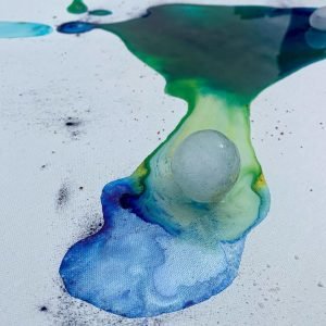 Vibrant abstract watercolor art with a translucent glass sphere on textured white canvas.
