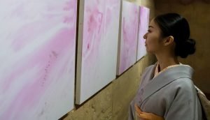 Elegant woman in kimono viewing abstract pink and white artwork at Sam Desmet gallery, contemporary art exhibition, cultural art event.