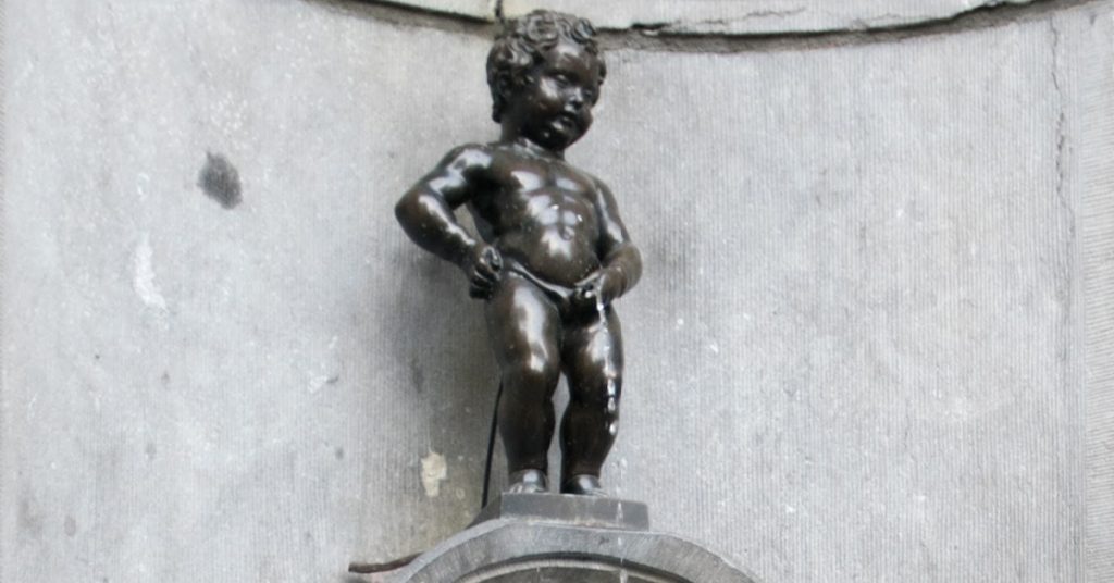Bronze statue of a playful, curly-haired boy standing confidently on a city street corner.