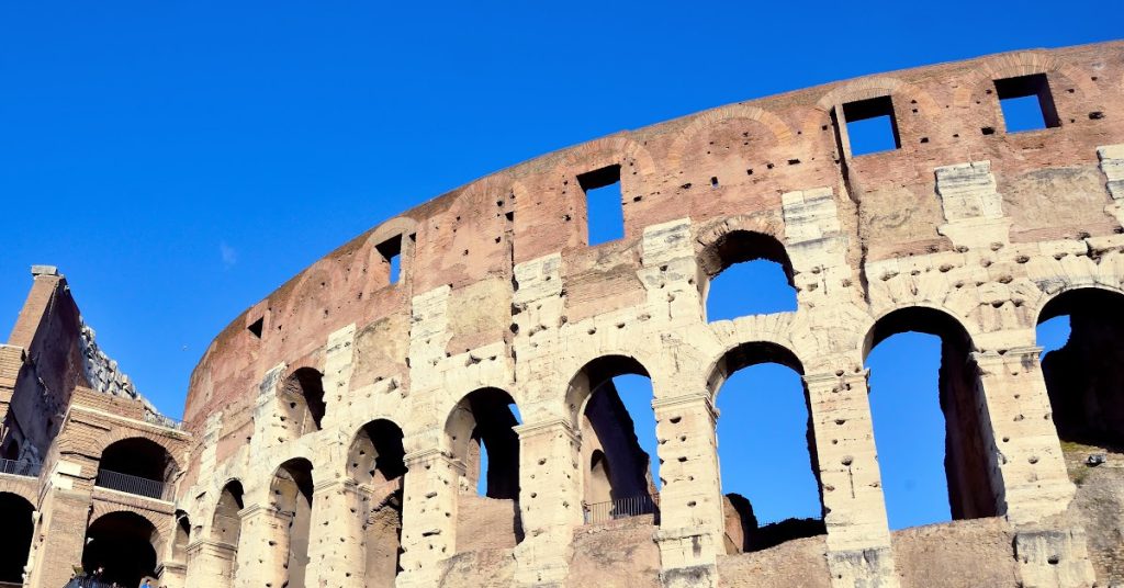 Ancient Roman Colosseum under bright blue sky, showcasing historic architecture and cultural heritage.