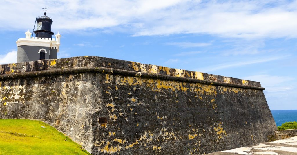 Lighthouse on historic stone fortress with blue sky and ocean background.