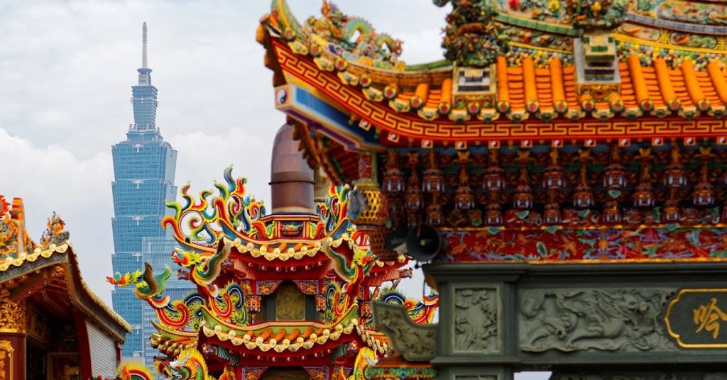 Colorful traditional Chinese temple architecture with Taipei 101 in the background, showcasing vibrant ornamentation and cultural heritage.