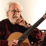 Elegant elderly man playing acoustic guitar in a cozy home studio setting.
