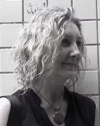 Lesley Oldaker with curly hair smiling, in an urban setting, portrait shot, black and white.