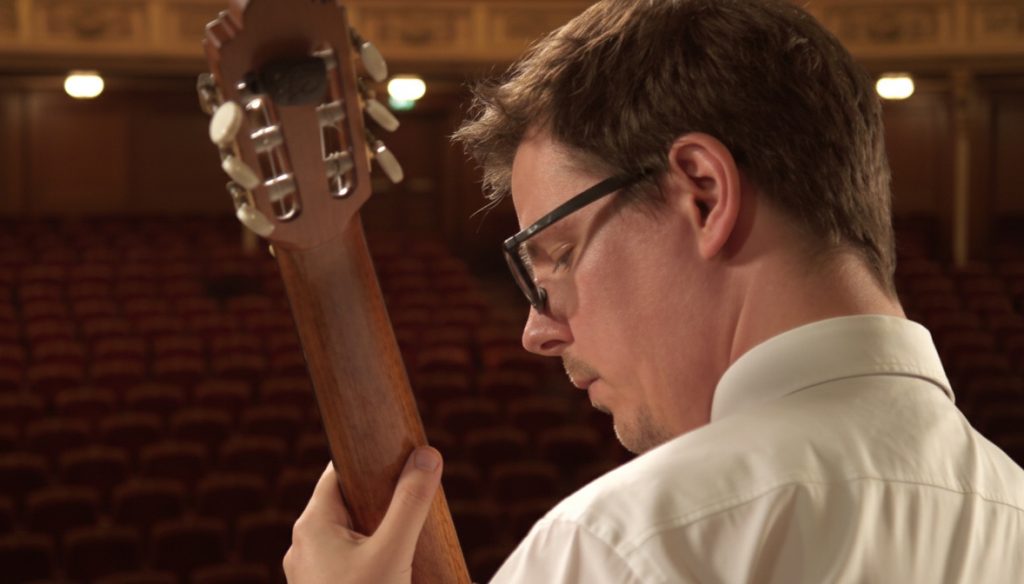 Close-up of Sam Desmet holding his classical guitar in a concert hall